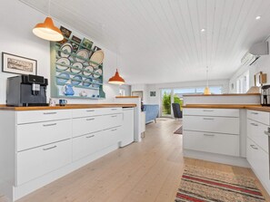 A modern kitchen with white cabinets, wooden countertops, and a central island. There are pendant lights above the island and a coffee machine on the countertop. - 4 Star Holiday Home in Bogense (Bogense)