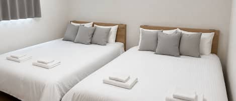 Two single beds with wooden headboards, white linens, and grey pillows.