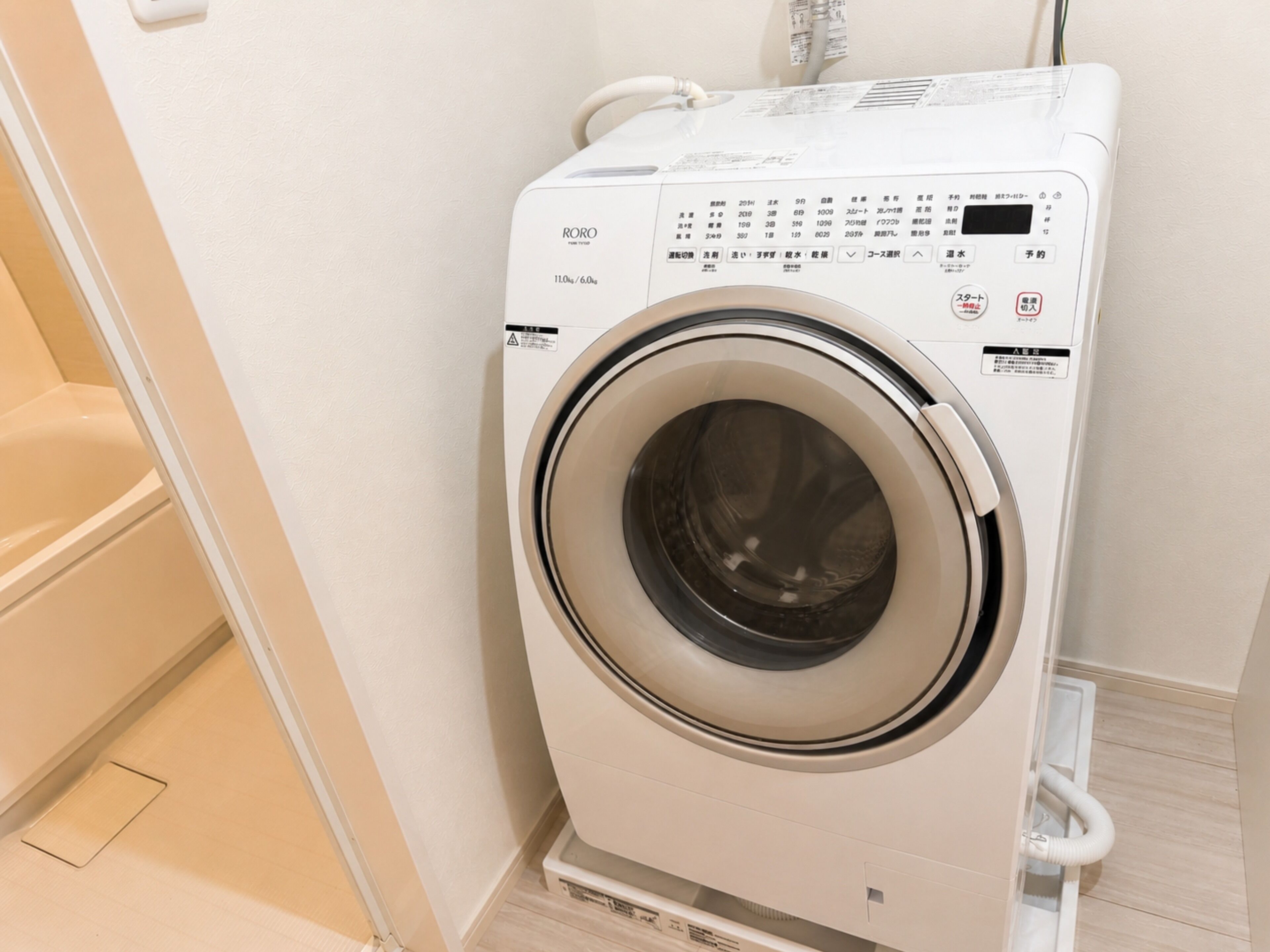 A front-loading washing machine in a bathroom with a tiled floor and a white wall.
