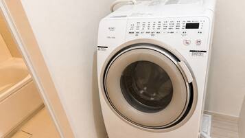 A front-loading washing machine in a bathroom with a tiled floor and a white wall.
