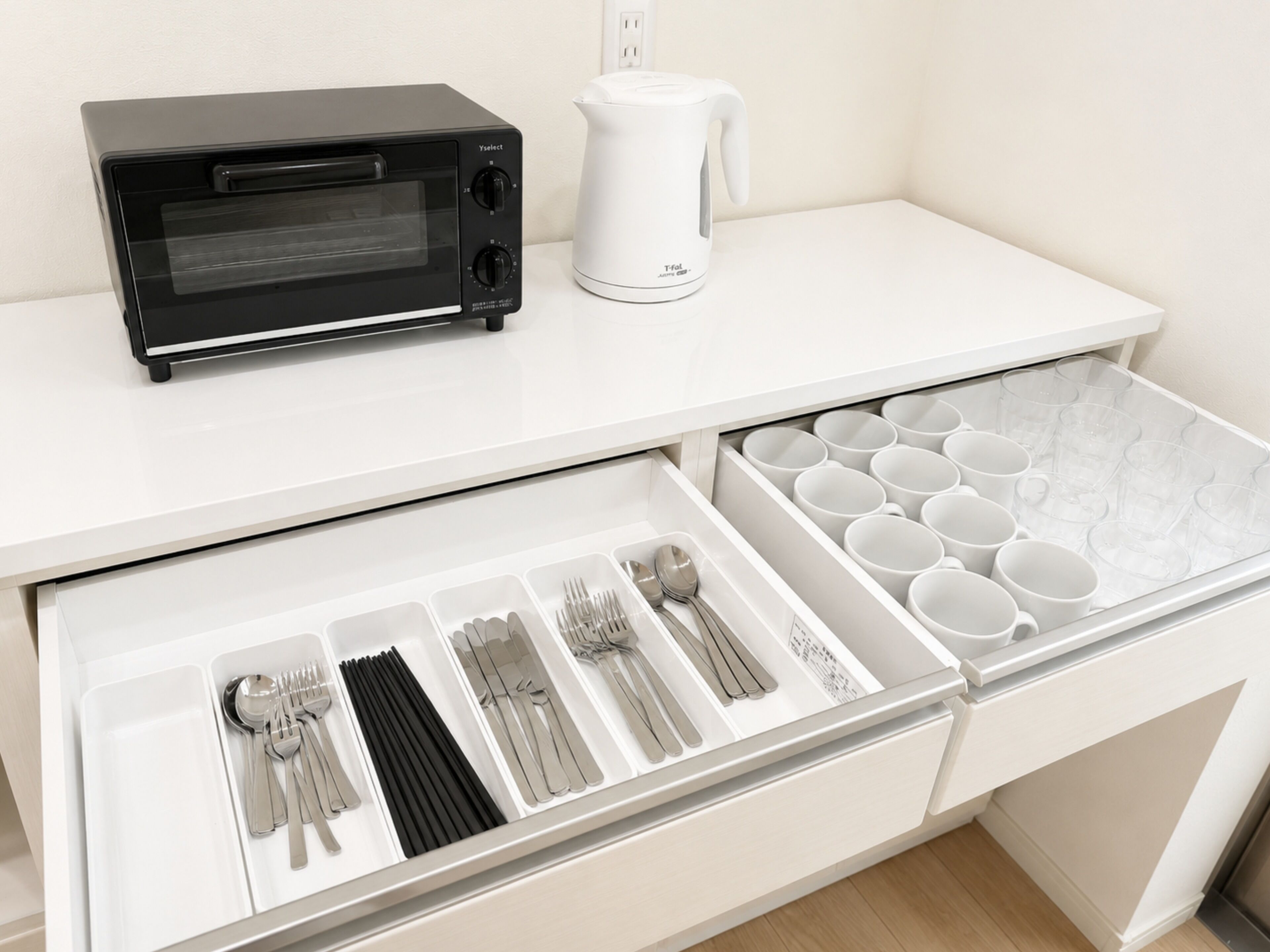 A kitchen with a toaster oven, kettle, and a drawer organizer with utensils and cups.