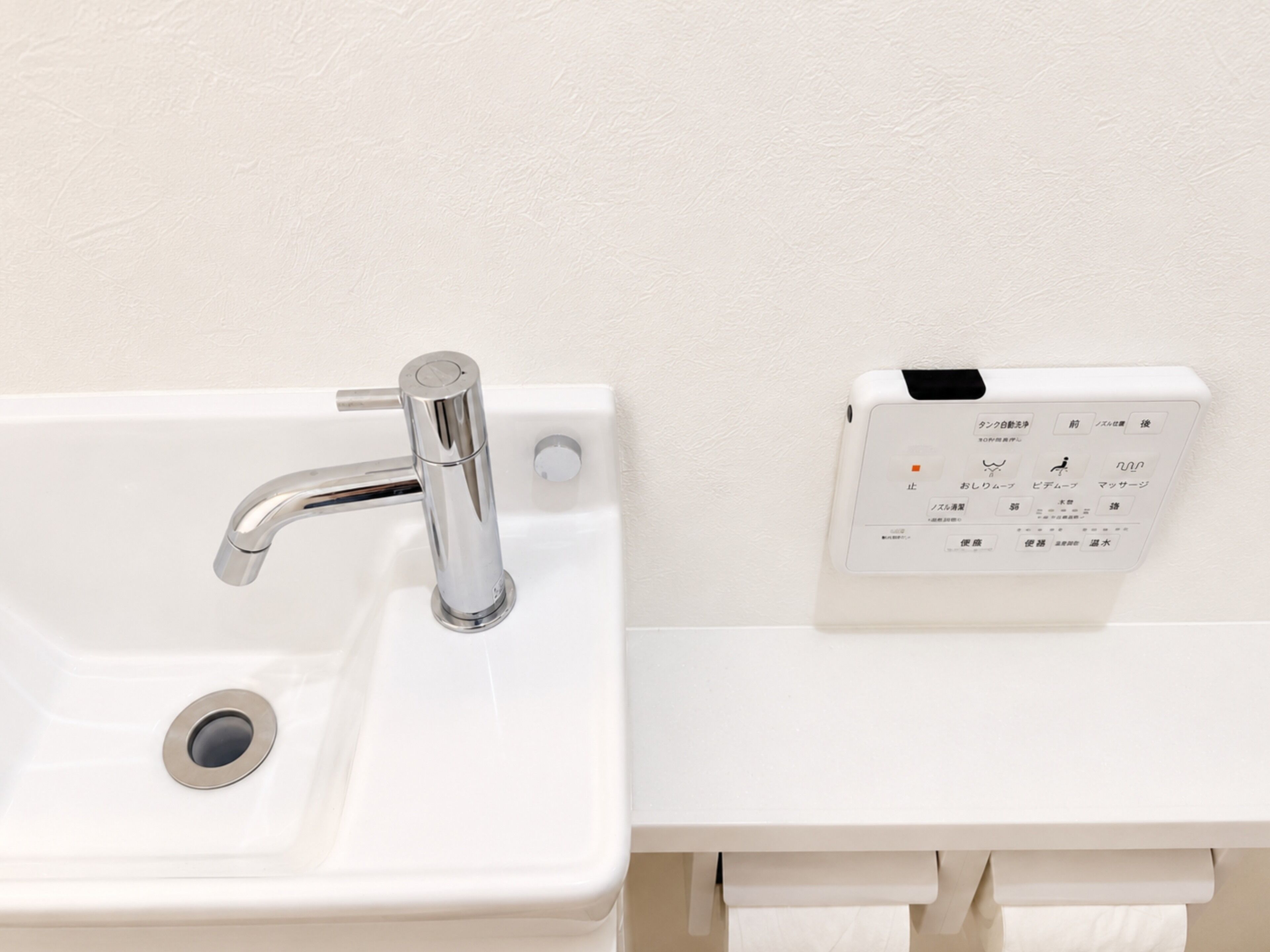 En hvid vask med en kromarmatur og et kontrolpanel med japansk tekst.