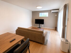 A compact room with a sofa, a small table, a TV, and an air conditioning unit. - NAKIJIN TERRACE (Heshiki Nakijinson)