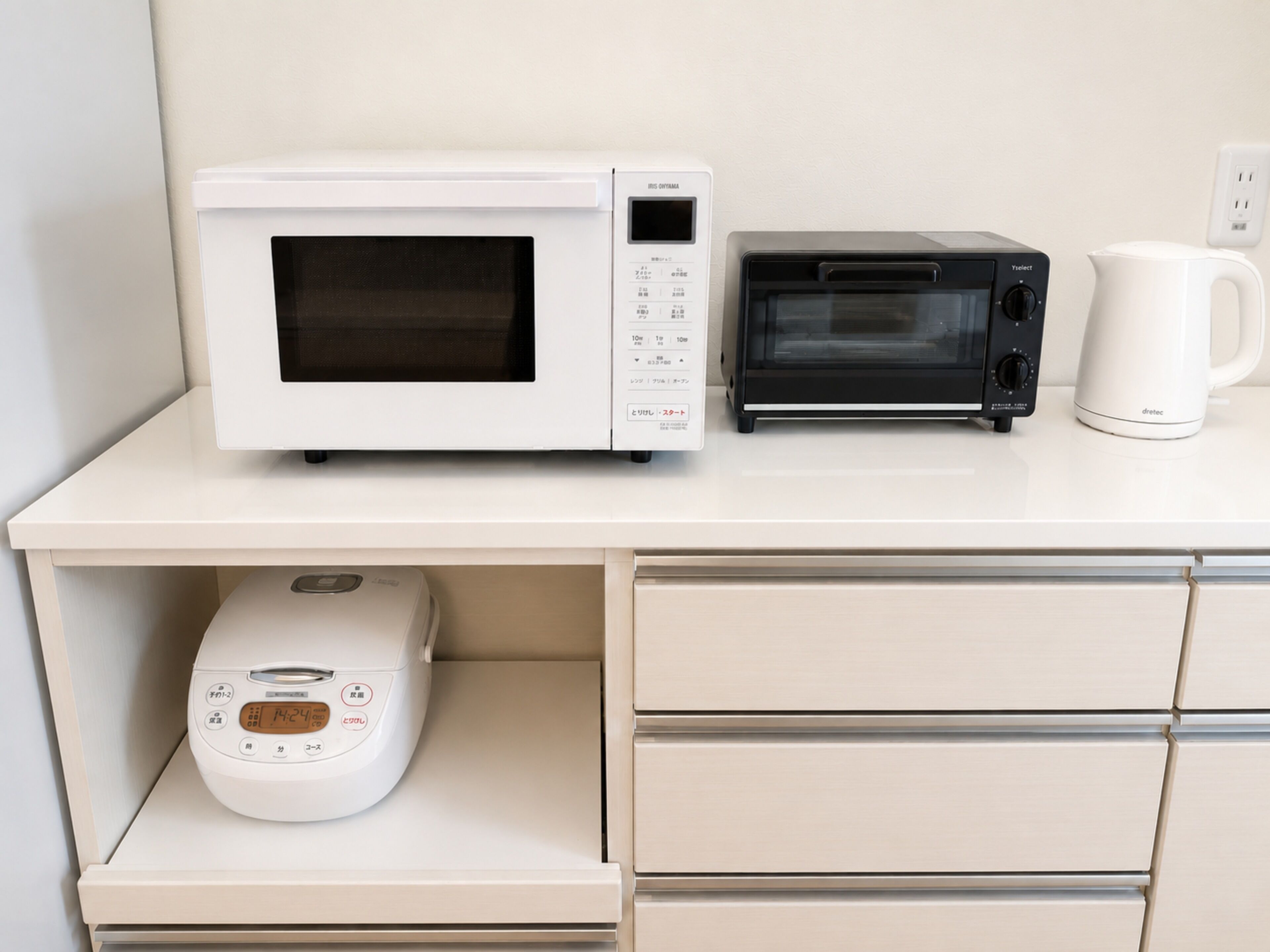 Una cocina con microondas, tostadora y cafetera sobre una encimera blanca.
