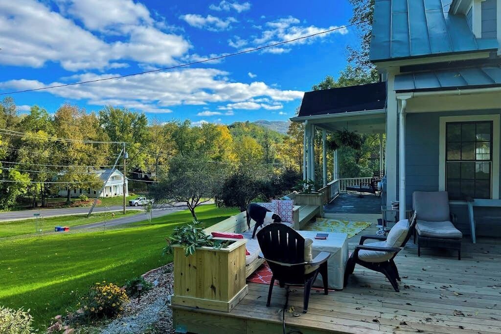 Une terrasse extérieure couverte, dotée de sièges, offrant une vue sur une pelouse verdoyante et, au loin, sur un bâtiment blanc.