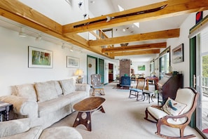 A spacious living room with a high ceiling, wooden beams, a sofa, a coffee table, and a piano. - Peaceful mountain home w/ amazing views; close to hiking trails & quaint towns (Franconia)