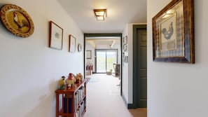 A hallway with framed pictures, a wooden console table with decorative items, and a door leading to a balcony. - Peaceful mountain home w/ amazing views; close to hiking trails & quaint towns (Franconia)