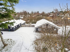 Ein mit Schnee bedecktes Anwesen mit zwei Gebäuden, einem eingezäunten Garten und blauem Himmel.