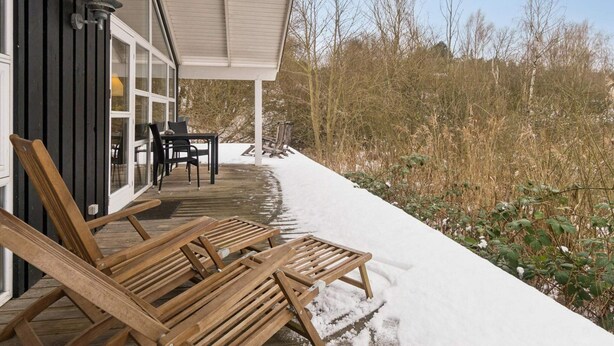 A wooden deck with lounge chairs, a table, and a building with large windows. - 4 Star Holiday Home in Knebel (Knebel)