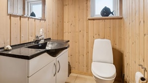 A wooden-paneled bathroom with a sink, mirror, toilet, and window. - 4 Star Holiday Home in Knebel (Knebel)