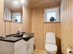 Ein Badezimmer mit Holzwänden, einem Waschbecken, einem Spiegel, einer Toilette und einem Fenster.