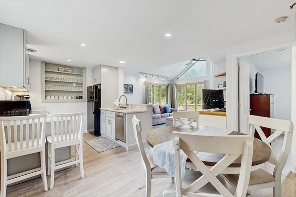 A modern kitchen with white cabinetry, a dining area with white chairs, and a large window providing natural light.