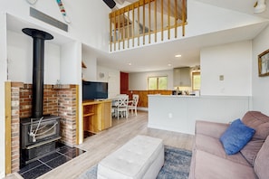 A spacious living area with a fireplace, a sofa, a television, and a kitchen in the background.