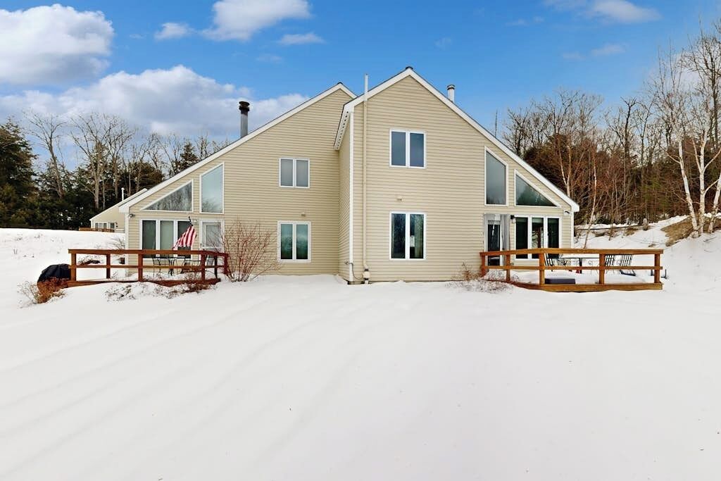 Een huis met twee verdiepingen, een ruime veranda, een schoorsteen en een oprit vol sneeuw.
