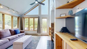 En moderne stue med en sofa, skammel og et stort fladskærms-tv på et træstel.