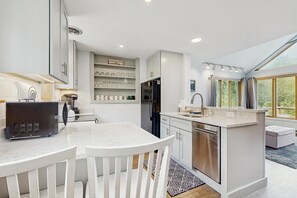 A modern kitchen with white cabinetry, a built-in island with a sink, and a dining area with white chairs.