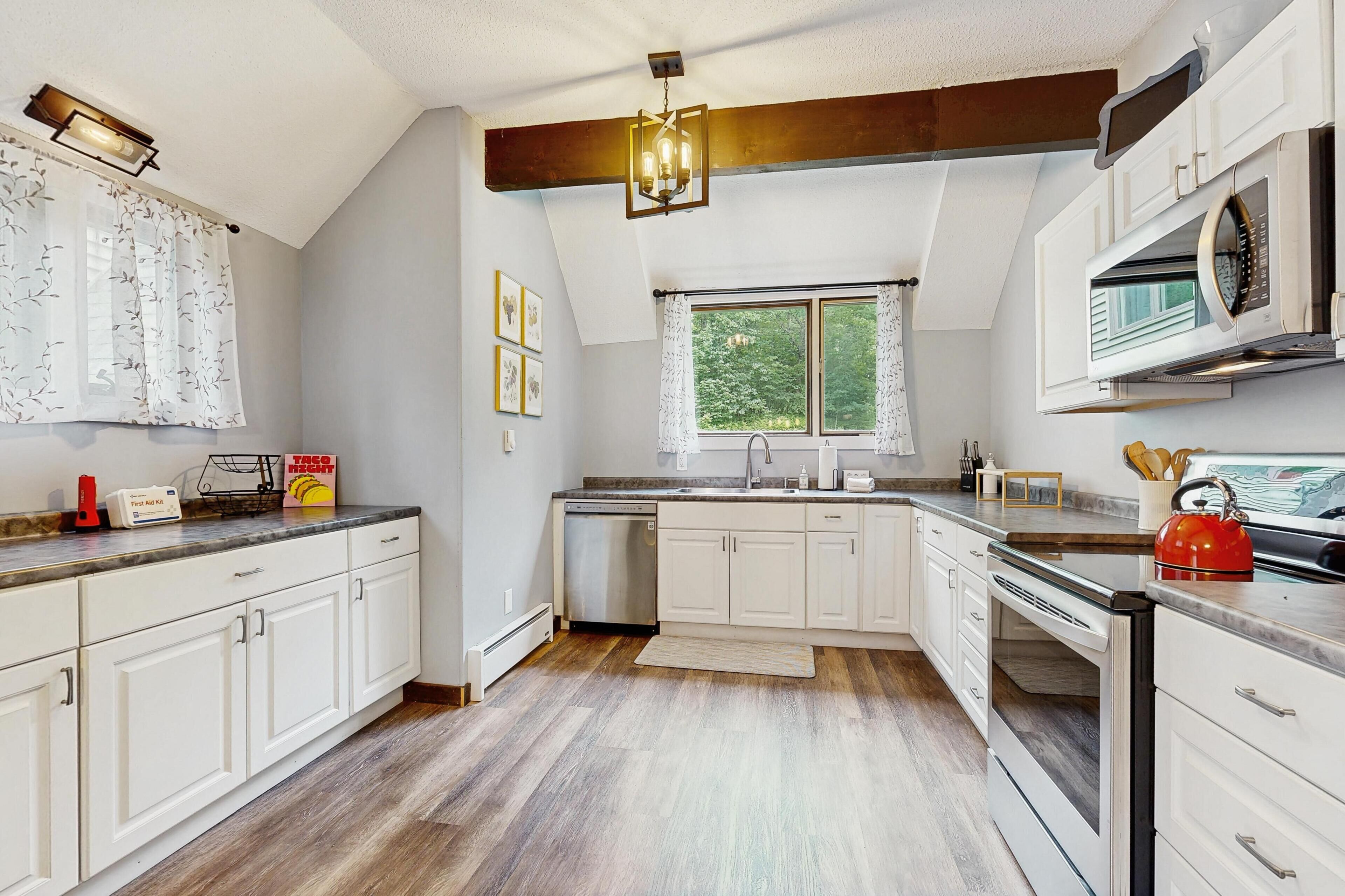 A kitchen with white cabinets, a dishwasher, a microwave, and a red kettle.