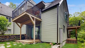 Ein zweistöckiges Haus mit einer Holzdielen-Terrasse, einem Balkon und einer Steinmauer.