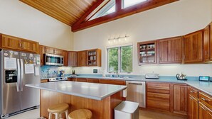 Une cuisine avec des meubles en bois, un réfrigérateur en acier inoxydable, un four à micro-ondes et un grand îlot central doté de tabourets.