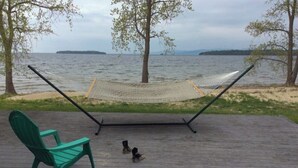 Un hamac sur une terrasse en bois, avec vue sur l’eau, et une chaise verte.