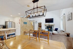 A modern kitchen with stainless steel appliances, a dining area with a wooden table and chairs, and a living room with a fireplace and a flat-screen TV. - Mt. Snow All Season Condo: w/ shared hot tub & pool, ski shuttle, tennis (Dover)