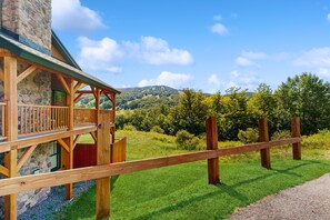 A wooden cabin with a stone exterior, a balcony, and a view of a green landscape with hills. - Newly renovated mountainside condo on the access road with two suites (Dover)