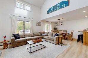 A spacious living room with a large sofa, a coffee table, and a dining area with a wooden table and chairs. - Newly renovated mountainside condo on the access road with two suites (Dover)