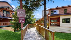 A wooden pathway leading to a building labeled 'Snow Mountain Village Sports Center' with a sign indicating 'SMV Owners & Guests Only' and 'Units 27A - 27E'.