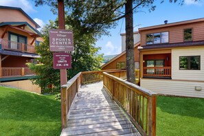 A wooden pathway leading to a building labeled 'Snow Mountain Village Sports Center' with a sign indicating 'SMV Owners & Guests Only' and 'Units 27A - 27E'.