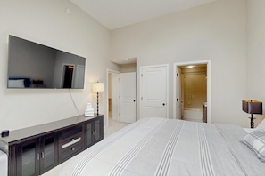 Ein Hotelzimmer mit einem großen Bett, einem Schminktisch, einem Spiegel, einem Flachbildfernseher und einem durchgegangenen Tür erkennbaren Badezimmer.