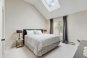 A bedroom with a skylight, a bed with a headboard, bedside tables with lamps, and a window with curtains. - Mt. Snow All Season Condo: w/ shared hot tub & pool, ski shuttle, tennis (Dover)
