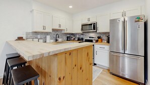 A modern kitchen with white cabinets, a stainless steel refrigerator, and a wooden island.