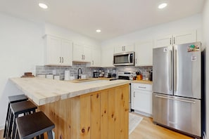 A modern kitchen with white cabinets, a stainless steel refrigerator, and a wooden island.