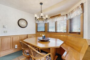 A dining area with a wooden table, chairs, a chandelier, and a wall clock. - Condo with gas fireplace and hiking trails at the door, near Story Land (Bartlett)