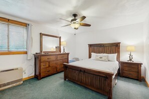 Quarto com cama de madeira, ventoinha no teto, cômoda e mesa de cabeceira com luminárias.