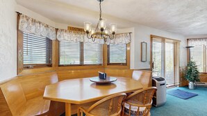 A dining area with a wooden table, two chairs, a chandelier, and large windows with blinds. - White Mountain Condo: close to ski, hiking, local attractions, dining & views (Bartlett)