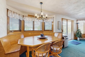 A dining area with a wooden table, two chairs, a chandelier, and large windows with blinds. - White Mountain Condo: close to ski, hiking, local attractions, dining & views (Bartlett)