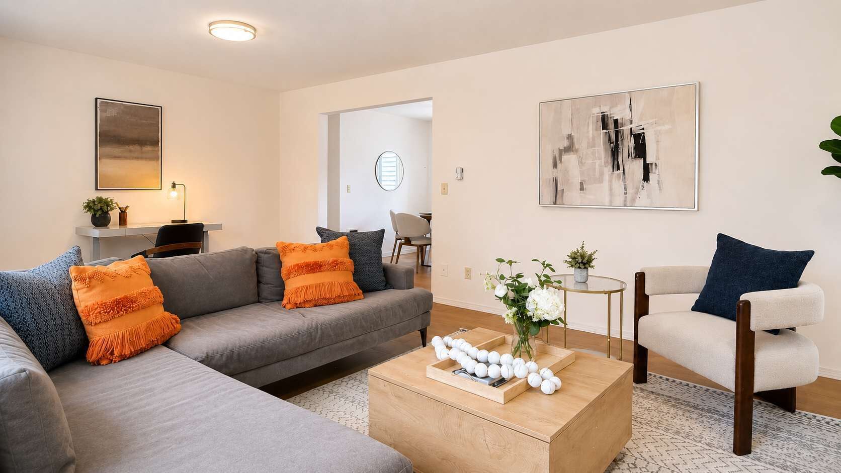 Een moderne woonkamer met een grijze bank, een witte fauteuil, een salontafel en een schilderij aan de muur.