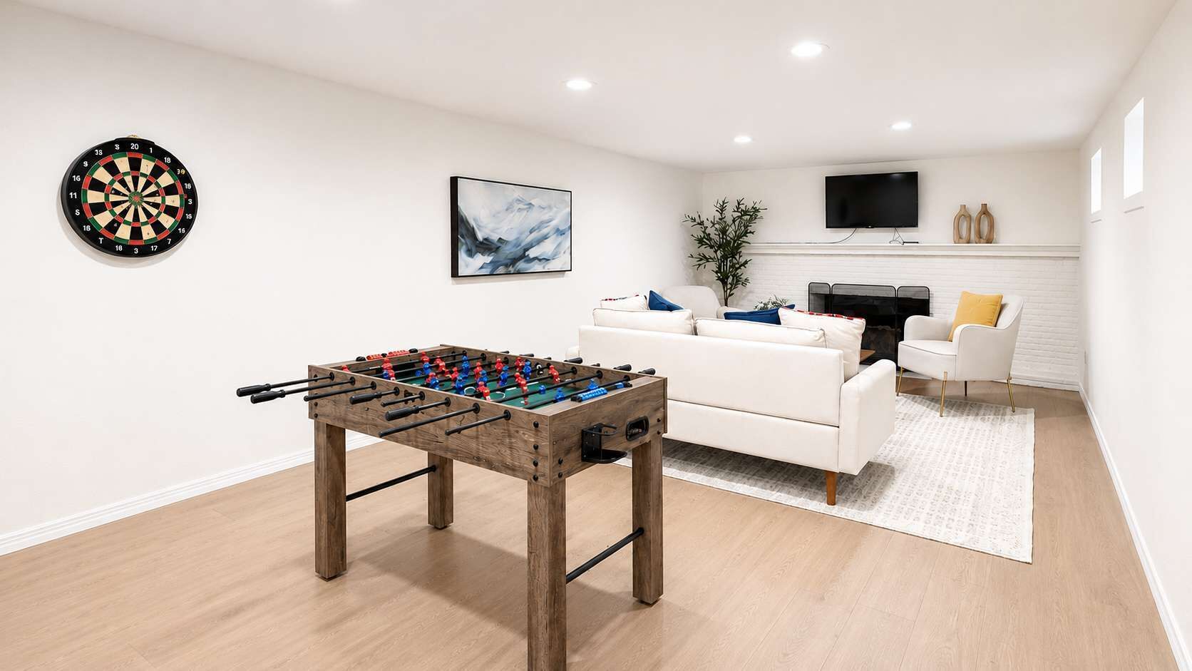 A living room with a foosball table, a dartboard, a sofa, a TV, and a fireplace.
