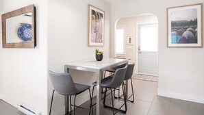 A dining area with a table, four chairs, a potted plant, and framed artwork on the walls.