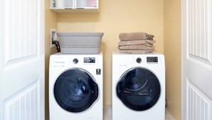 Two front-loading washing machines, a white laundry basket, and a stack of folded towels in a laundry room with a beige wall and white doors.