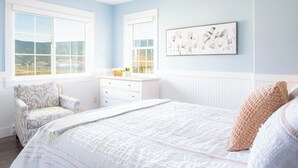 A bedroom with a large bed, a chair, a dresser, and a window with a view.