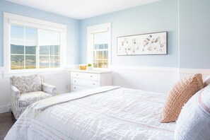 Ein Schlafzimmer mit einem großen Bett, einem Sessel, einer Kommode und einem Fenster mit Blick.
