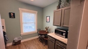 A compact kitchen with a dining table, a microwave, cabinets, and a window with blinds. - Sherman Hills Historic Retreat #6 (Des Moines)