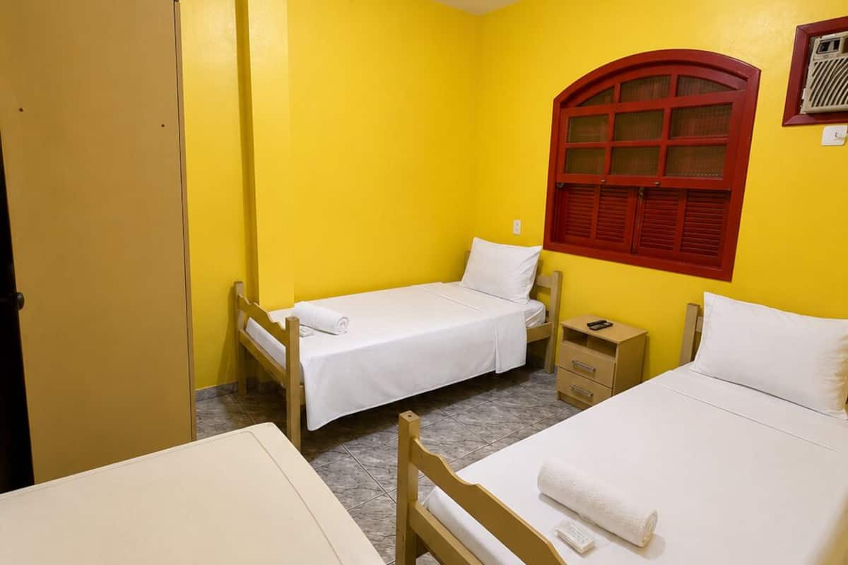 Ein Hotelzimmer mit zwei Einzelbetten, einem Kleiderschrank, einem Schreibtisch und einem Fenster mit Rollläden.