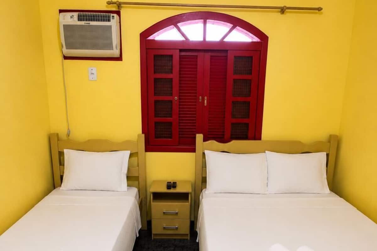 Ein Zimmer mit zwei Betten, einem roten Fenster und einer Klimaanlage.