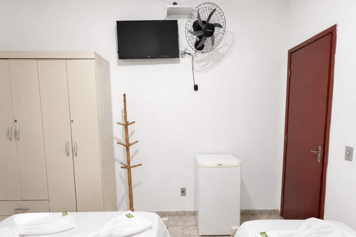 Ein Hotelzimmer mit zwei Betten, einem Fernseher, einem Ventilator, einem Kleiderschrank und einem Badezimmer.