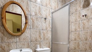 Un baño con pared de azulejos de mármol, un espejo redondo, un lavamanos, un inodoro y una ducha.