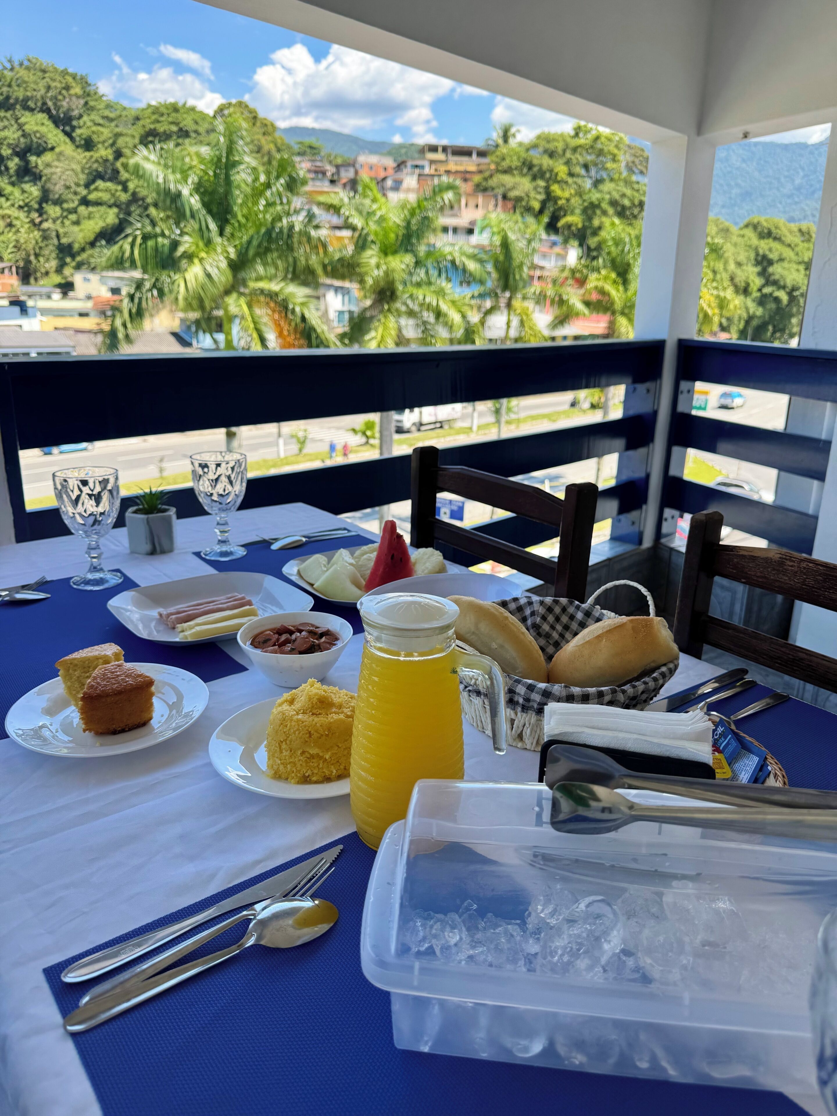 Una mesa dispuesta con comida y bebidas, con vistas a un paisaje urbano y zonas verdes.