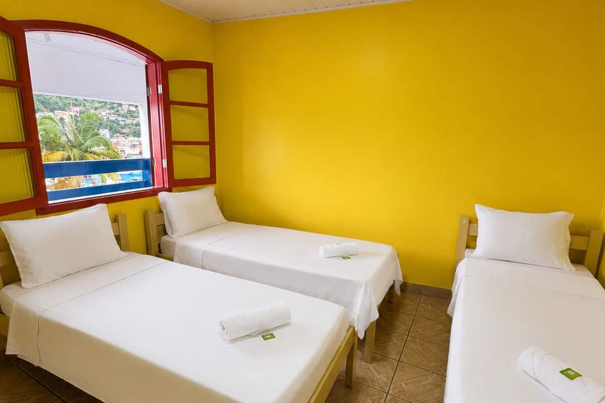 Ein Hotelzimmer mit drei Einzelbetten, einem Fenster mit Blick und einem gefliesten Boden.